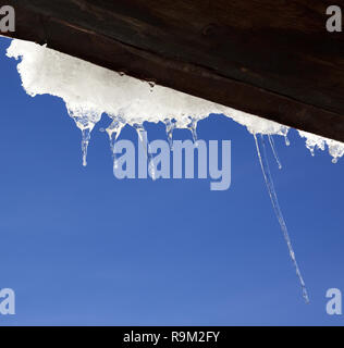 Wooden roof with snow cornice and icicles at sun winter day. Bottom view. Stock Photo