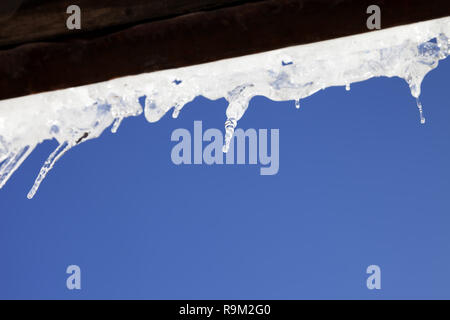 Wooden roof with snow cornice and sunlight icicles at sun winter day. Bottom view. Selective focus. Stock Photo