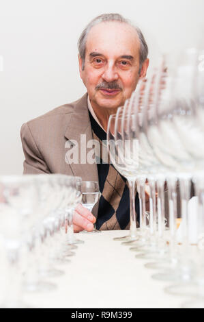 Man sitting and holding glass shot with Vodka on background and rows of empty wineglasses and shots standing on the table in front of him Stock Photo