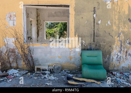 Grungy wallpaper background of yellow abandoned construction with windows showing nature and a green worn sofa in front of it. No people. Stock Photo