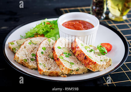 Tasty homemade ground  baked chicken meatloaf with green peas and broccoli on black table. Food american meat loaf. Stock Photo
