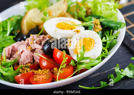 Healthy hearty salad of tuna, green beans, tomatoes, eggs, potatoes, black olives close-up in a bowl on the table. Salad Nicoise. French cuisine. Stock Photo