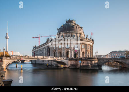 Bode Museum with the river Spree at blue sky. Historic bridges across the river to Museum Island with smooth water surface. TV tower in the background