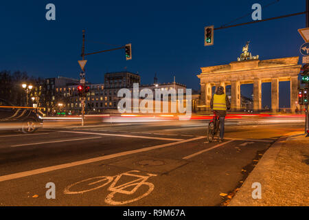 Brandenburg gate at night. Backside view in the street with cyclists and light of cars at long time exposure. Bicycle path with sign on the asphalt. Stock Photo