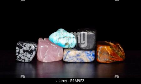 A stack of semi-precious gemstones reflecting on a black shiny surface against a black background. Stock Photo