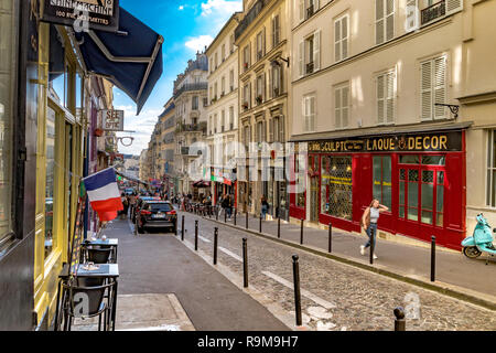 A  French flag hangs outside a shop as a woman walks along Rue des Martyrs, a narrow street in Montmartre, Paris, France Stock Photo