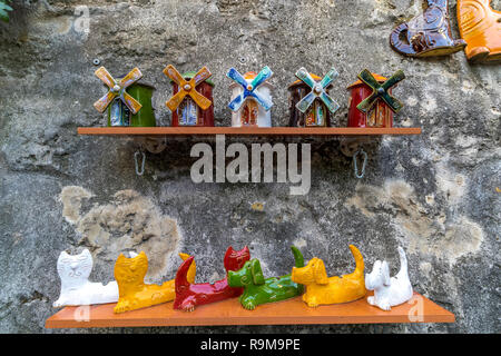 Souvenirs of Montmartre including Ceramic windmills and ceramic cats and dogs on a wooden shelf fixed to a stone wall Stock Photo