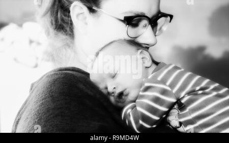 New Mother Holds Newborn Baby Boy Wrapped in a Blanket As He Sleeps on her Chest. Black & White Photo. Stock Photo
