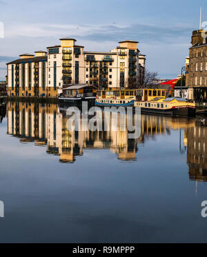 The Shore, Leith, Edinburgh, Scotland, UK. 26th Dec, 2018.  UK Weather: A brighter Boxing Day ends with sun reflected off the windows of apartments of the modern development of Queen's Quay on the riverbank of the Water of Leith, and buildings and barges colourfully reflected in the water Stock Photo