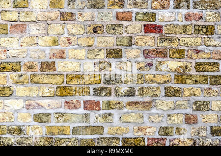 Old brick wall with grey mortar and with relatively large blocks in various shades of red, yellow and brown Stock Photo