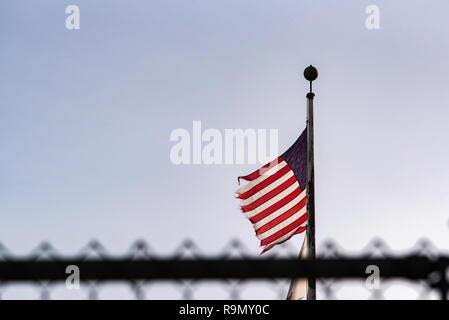 A frayed and worn American (USA) flag flies above a wire fence Stock Photo