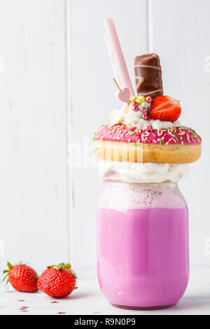 Pink strawberry Freak Shake cocktail with donut and sweets on a white background, copy space. Unhealthy desserts concept. Stock Photo