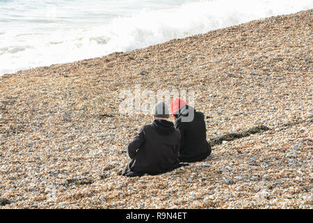 A couple sitting on the beach on Brighton seafront, East Sussex, England, UK Stock Photo