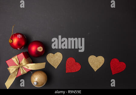 Christmas and love. Top view of red and golden hearts, a gift box with red ribbon and a christmas balls, black background, copy space, Stock Photo