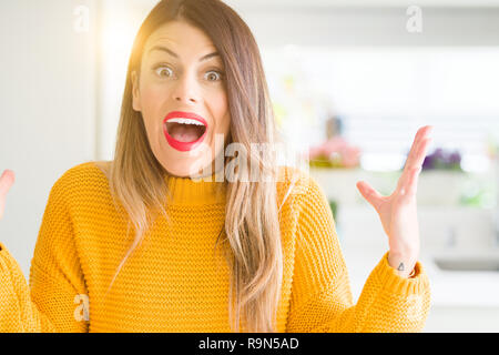 Young beautiful woman wearing winter sweater at home celebrating crazy and amazed for success with arms raised and open eyes screaming excited. Winner Stock Photo