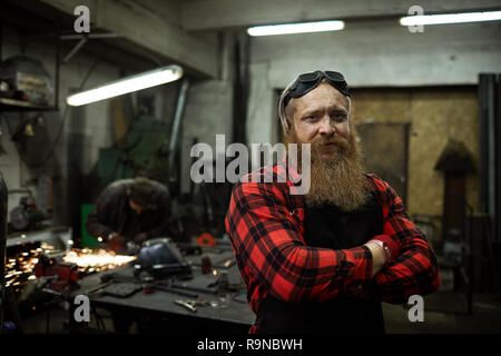 Content blacksmith in safety goggles on head in welding shop Stock Photo