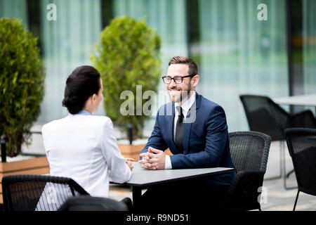 Smiling man and woman sitting at cafe and having dialogue Stock Photo