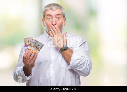 Handsome senior man holding bunch of money over isolated background cover mouth with hand shocked with shame for mistake, expression of fear, scared i Stock Photo