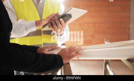 Men and woman meeting in construction site. Teamwork with foreman speaking with engineer holding blueprints. Focus on wedding ring on female's hand. C Stock Photo