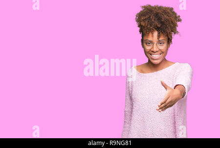 Beautiful young african american woman wearing glasses over isolated background smiling friendly offering handshake as greeting and welcoming. Success Stock Photo