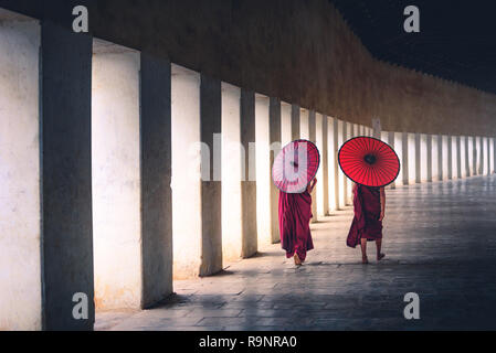 Two buddhist monk novice holding red umbrellas and walking in pagoda, Myanmar. Stock Photo