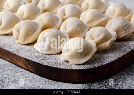 Uncooked russian pelmeni on cutting board and ingredients for homemade pelmeni on white table. Process of making pelmeni, ravioli or dumplings with me Stock Photo