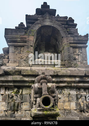 carved stormwater spout below a headless sitting Buddha statue in a niche at 9th century Borobudur Mahayana Buddhist temple, Central Java, Indonesia Stock Photo
