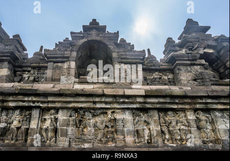 bas-relief panels with narratives of Buddhist mythology and life in Java of the period below niches with sitting Buddha statues on the terraces of 9th Stock Photo