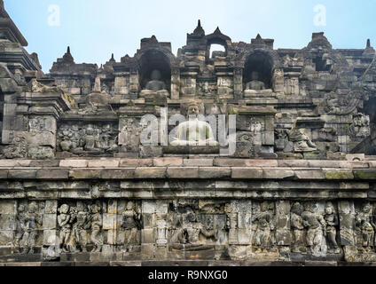 bas-relief panels with narratives of Buddhist mythology and life in Java of the period below niches with sitting Buddha statues on the terraces of 9th Stock Photo