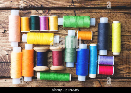 Colored spools of thread laid out in rows on wooden background Stock Photo