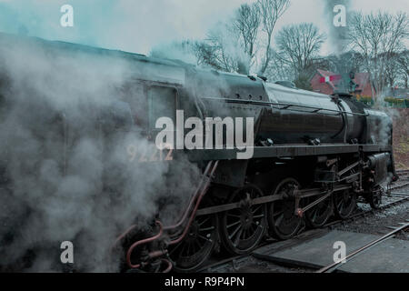 Nostalgic and atmospheric steam train. Full head of steam as it passes through a railway station. Lots of steam partially obscuring the Engineer. Stock Photo