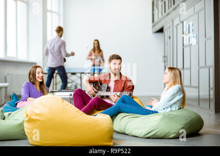 Group of a young coworkers having fun playing guitar and playing small tennis during the coffee break in the office Stock Photo