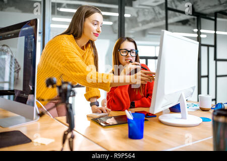 Two young creative women dressed in sweaters working with computer in the modern office Stock Photo