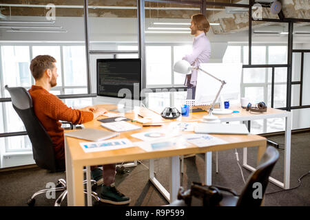 Man as a programmer working with computer code sitting at the beautiful working place in the modern office interior Stock Photo