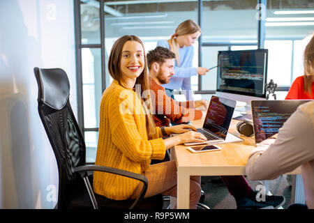 Team of a young woman as a programmer sitting in the office with people working on the background Stock Photo