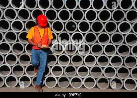 Construction worker leaning on cement pipes at worksite, USA Stock Photo