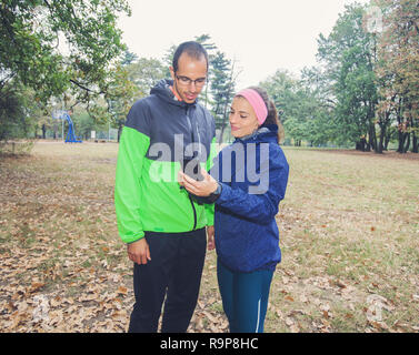 Fitness young woman show to sporty man on the smartphone, plan for exercising in forest. Sporty woman and men prepare for workout. Stock Photo