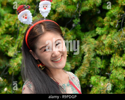 Smiling young Thai woman with a Christmas headband and jingling Christmas earrings poses for the camera. Stock Photo