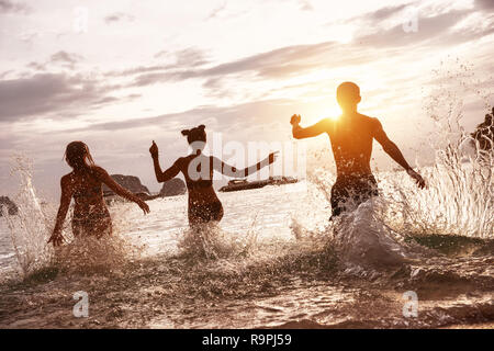 Group of happy friends run and jump at sunset sea beach. Tropical vacations concept Stock Photo