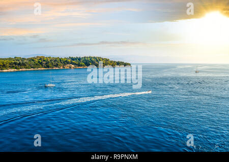 Two small sailboats in the Aegean Sea head towards the setting sun beaten Greek islands off the coast of Corfu, Greece. Stock Photo