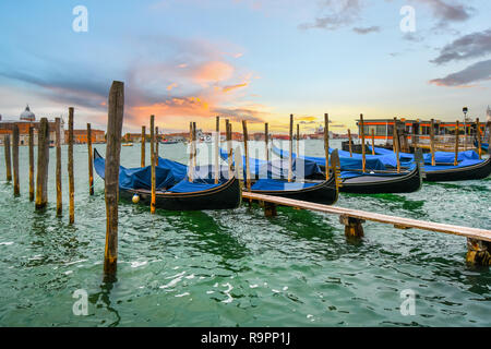 Gondolas line up at the pier along the grand canal as the sun sets in Venice, Italy Stock Photo