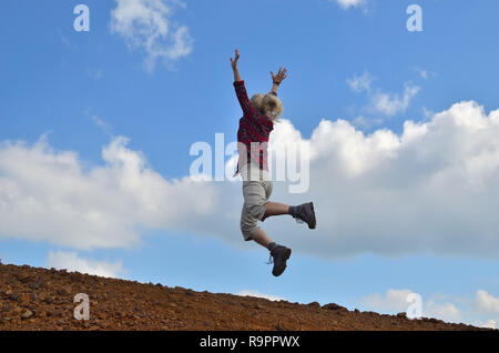 Happy woman, dressed in royal stewart, jumping against the blue sky with white clouds Stock Photo