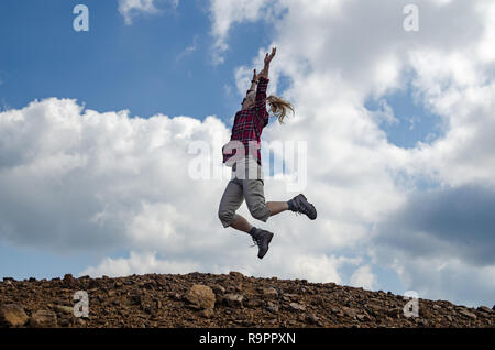 Joyful woman, dressed in royal stewart, jumping with spread arms. Sky and clouds are in background. Stock Photo