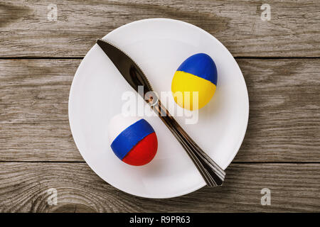 Two Easter eggs painted in the color of the flags of Russia and Ukraine in a plate on a wooden table, top view Stock Photo