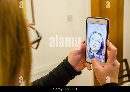 a lady takes a selfie using Snapchat on an iPhone which augments the image with effects Stock Photo