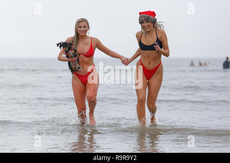 Pictured: Two young women in bikinis and Santa hats run in the sea.  Tuesday 25 December 2018 Re: Hundreds of people take part in this year's Porthcaw Stock Photo