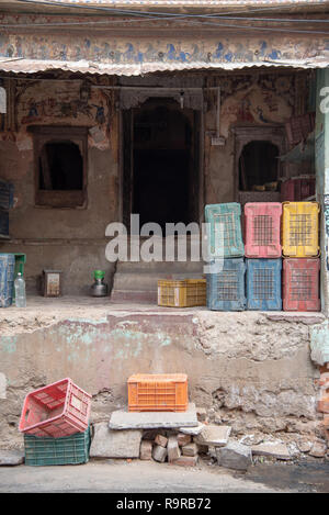Multi-coloured empty crates stacked at the entrance of a run down and crumbling dwelling in Bikaner, Rajasthan, INDIA Stock Photo