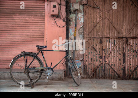 Old bike stood against a rusted pink shuttered backdrop.  Old City, Jaipur, Rajasthan, INDIA. Stock Photo