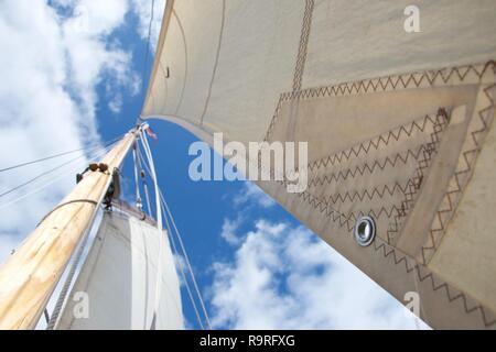 Looking up the mast on a traditional gaff rigged yacht / sailing boat. The focus is on an eyelet in the jib (smaller sail). The sky is blue with littl Stock Photo