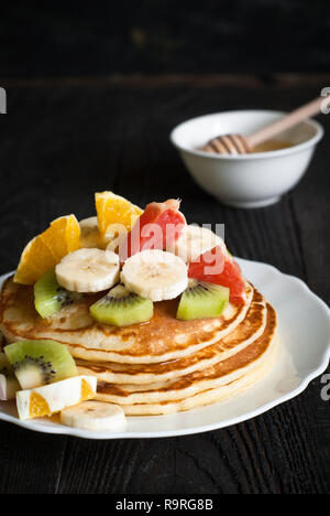 Plate of pancakes with fruits and honey at dark wooden table. Stock Photo